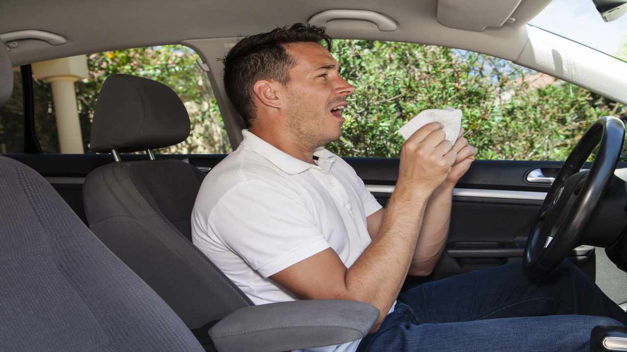 Uomo che starnutisce in auto per allergia 